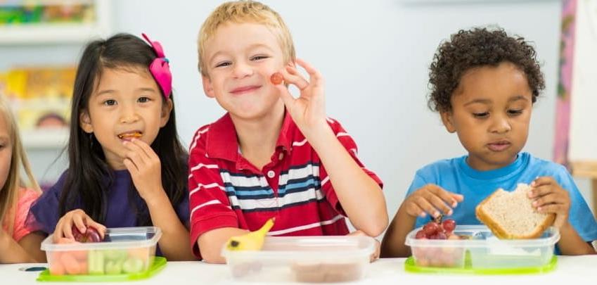 three children at a table smiling and eating healthy food